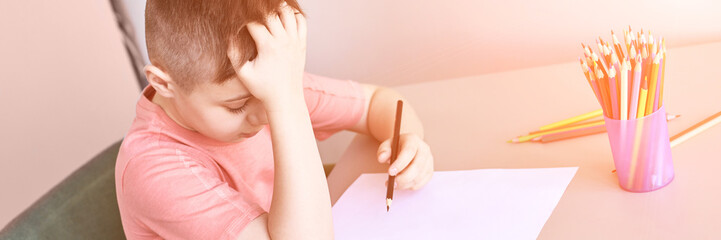 Little boy drawing. Closed Locking Exercise. Homemade routine. School lessons. Write pencil on piece of paper. Home study. Elementary preschool. Male kid student. Thinking or dreaming. Horizontal