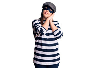 Young beautiful brunette woman wearing burglar mask sleeping tired dreaming and posing with hands together while smiling with closed eyes.