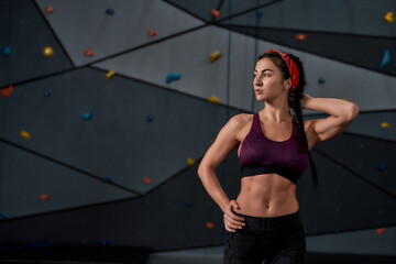 Active young woman in sportswear looking aside, standing against artificial training climbing wall. Concept of sport life and rock climbing