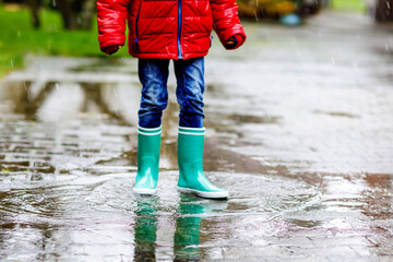 Close-up of kid wearing yellow rain boots and walking during sleet, rain and snow on cold day. Child in colorful fashion casual clothes jumping in a puddle. Having fun outdoors