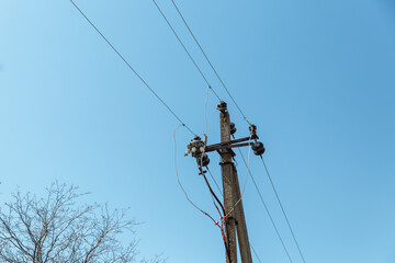  Power line post with electricity cables against a clear sky with white clouds. A tree grows near a...