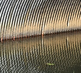 Reflection of interior wall of drainage culvert on water.  Interesting vertical lines and ripples.