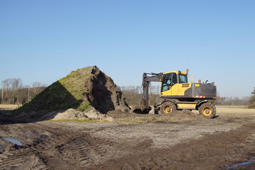 Yellow excavator and a heap of soil near a flower bulb field in winter in the Dutch village of Egmond aan den Hoef. Netherlands, February