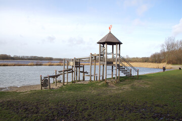 View of the lake from the Geestmerambacht recreation area near the Dutch city of Alkmaar. There is a wooden climbing frame in the grass on the bank. Netherlands, February 18, 2020      