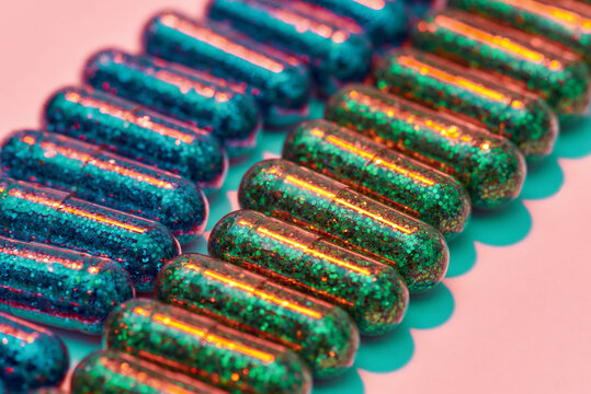 Creative concept with many green and blue glitter pills lying in two rows isolated on pastel pink background. Minimal style, art concept