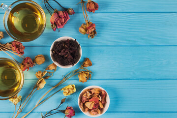 Top view on fresh rose floral tea, organic herbal infusion in two glass cups with dry rosebuds and petals around on blue wooden background with copyspace - alternative folk medicine and relax concept