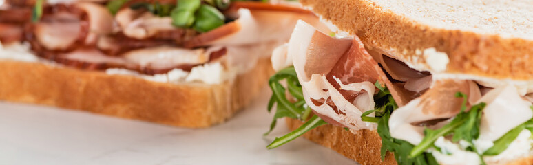 selective focus of fresh sandwich with arugula and prosciutto on white surface, panoramic shot