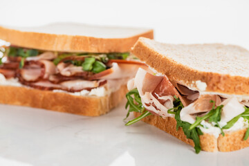 selective focus of fresh sandwich with arugula and prosciutto on white surface