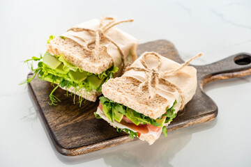fresh green sandwiches with avocado and meat on wooden cutting board on white surface
