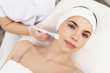 Model in white headband bandage cap lying on couch with closed eyes. Hand of beautician doctor in white glove touching her face with brush. Head and shoulders, healthcare, cosmetology, beauty clinic