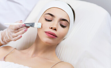 Model in white headband bandage cap lying on couch with closed eyes. Hand of beautician doctor in white glove touching her face with brush. Head and shoulders, healthcare, cosmetology, beauty clinic
