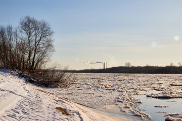 Fototapeta na wymiar Ice drift on a river with blue high water and big water, white snow broken ice full of hummocks in it and tree branches in the foreground in sunny spring day.