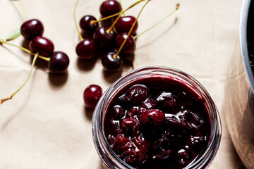 Cooked homemade cherry jam in the bowl and in the jar, raw cherries near on the table, organic meal and dessert concept