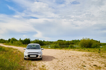 Small car standing on the side of road near wate of lake, river, fiord, sea and ocean.