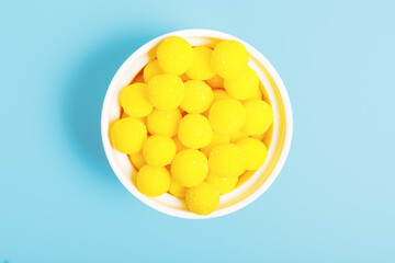 Yellow round candies in a white bowl on a blue background. concept of unhealthy food with sugar. sweets concept for kids. sweets store concept. top view, minimalism.