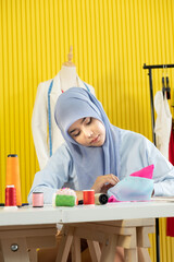 A young beautiful Asian Muslim woman designer who wore a hijab as a startup business owner is sewing the colorful fabric on her working table.