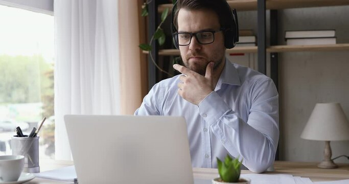 Serious man wear headset look ap pc screen writes ideas questions do review make research sit at desk. Businessman learn language improve knowledge, self-education, modern tech educational app concept