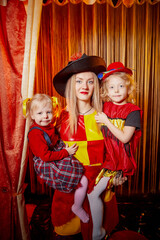 Family with dog during stylized theatrical circus photo shoot in beautiful red location. Model mother and young daughter with small animal posing on stage with curtain