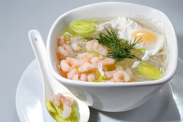 Soup with shrimp, rice noodles and egg in a white bowl on a gray background