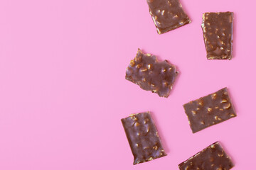 pieces of chocolate with nuts on a pink background. sweets store concept. Beautiful background for the designer. top view, copy space, flat lay. minimalism.