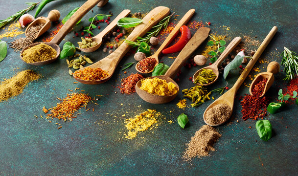 Various spice and dried herbs on dark green background. Top view of spices in wooden spoons