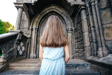 A little girl child in a dress goes up the steps to the door of a beautiful fairy-tale castle, a...