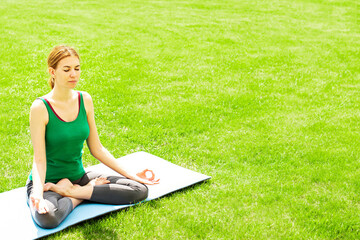 A woman practices yoga outdoors on the grass. Copy space