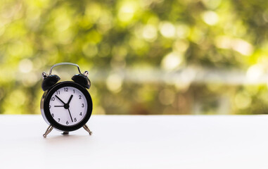 Mini alarm clock against natural blurred green background. Time change concept. Space for text