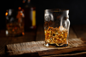 Glass of whiskey with ice on wooden table.