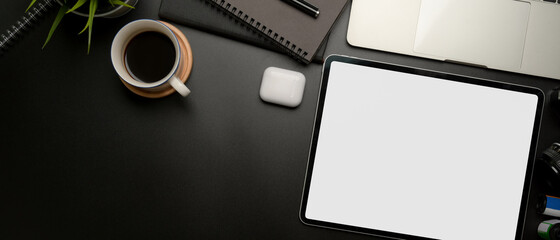 Blank screen tablet on dark modern workspace with copy space, coffee cup and office supplies