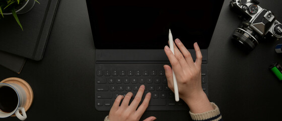 Hands using digital tablet with stylus on dark modern office desk with camera and supplies