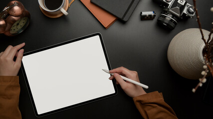 Female worker using blank screen tablet with stylus on dark luxury office desk with camera,...