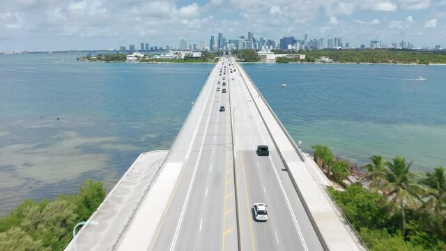 Beautiful aerial view of the automotive bridge over the Atlantic ocean bay at sunny day. 4K drone shot of cars driving above the beautiful blue waters in direction of Miami downtown, Florida, USA.