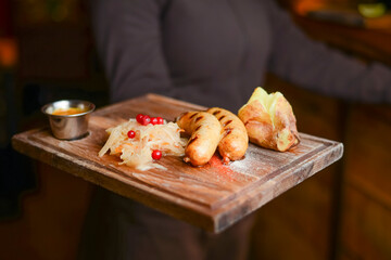 Baked potato with sausages and cabagge salad with sauce served on a wooden cutting board in a restaurant or cafe.
