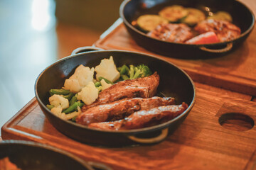 Delicious grilled marinated steaks and roasted vegetables from a summer BBQ on a wooden board in a restaurant.