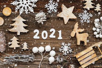 White Letters Building The Word 2021. Wooden Christmas Decoration Like Tree, Sled And Star. Brown Wooden Background With Snowflakes