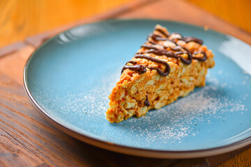 A piece of anthill cake with chocolate served on a blue plate over rustic wooden table. Sweet delicious dessert.
