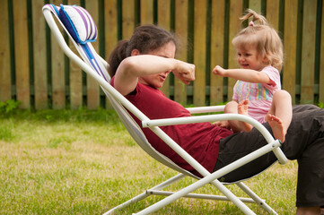 Mother and baby having fun. High five. Backyard. Mother and little daughter daughter sitting in deckchair. People sitting in sun lounger. Happy family