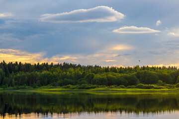 Fototapeta na wymiar Beautiful evening landscape with a forest lake. Picturesque view of trees on the lake shore and clouds in the sky.