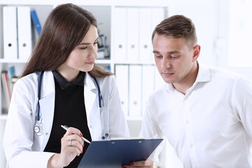 Smiling beautiful female medicine doctor explain diagnosis to male patient in business suit holding...