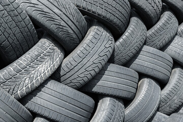 Old used weared car and truck wheels tyres pile stacked in rows stored for recycling. Heap of many rubber tires wall background. Idustrial pollution of environment