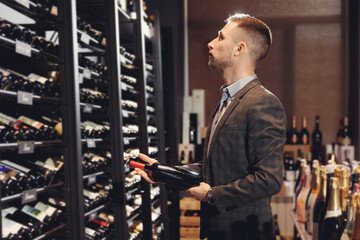 Fototapeta na wymiar Sommelier takes bottle of red wine from counter of restaurant drinks store