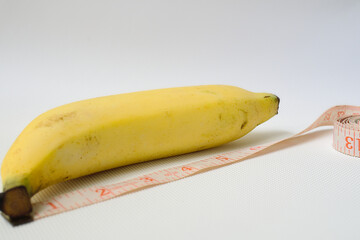 Penis size concept using yellow banana, soft measuring tape in white background