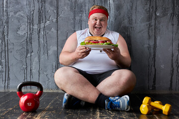 obese young caucasian man encroaches on a big sandwich, fat man can not adhere to a healthy...