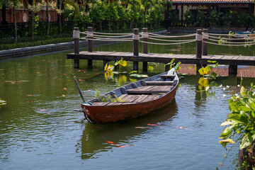 Obraz premium Wooden boat on the pond near the pier in a tropical garden in Danang, Vietnam