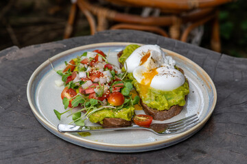 Healthy breakfast with bread toast and poached egg with green salad, red tomato and smashed avocado