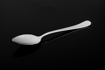 Studio photography of a teaspoon on a black reflective surface. stainless steel spoon