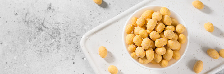 Fried peanuts in cheese sauce in a white bowl on a light gray table. Banner with space for text