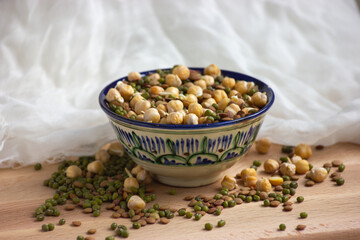 Sprouted chickpeas, lentil and mung beans in colourful bowl on wooden and white textile background. Front view.