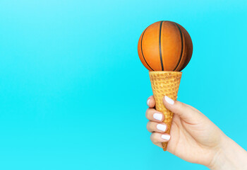 Female hand holds ice cream cone with basketball, creative summer background.